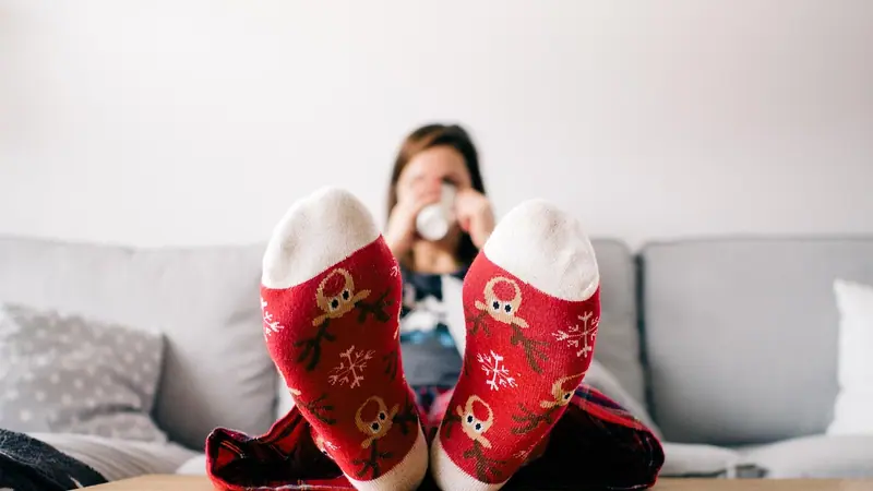 Pés com meias vermelhas apoiados na mesa de centro, com uma pessoa relaxando no sofá ao fundo