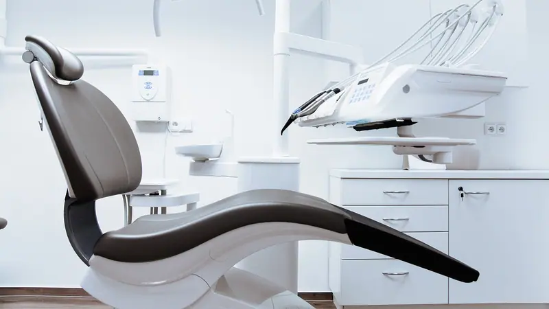 Cadeira odontológica moderna em consultório claro, com refletor e armários brancos