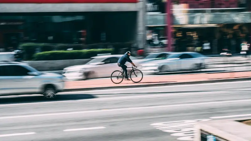 Carros e um ciclista passando em movimento por uma avenida, com efeito de borrão