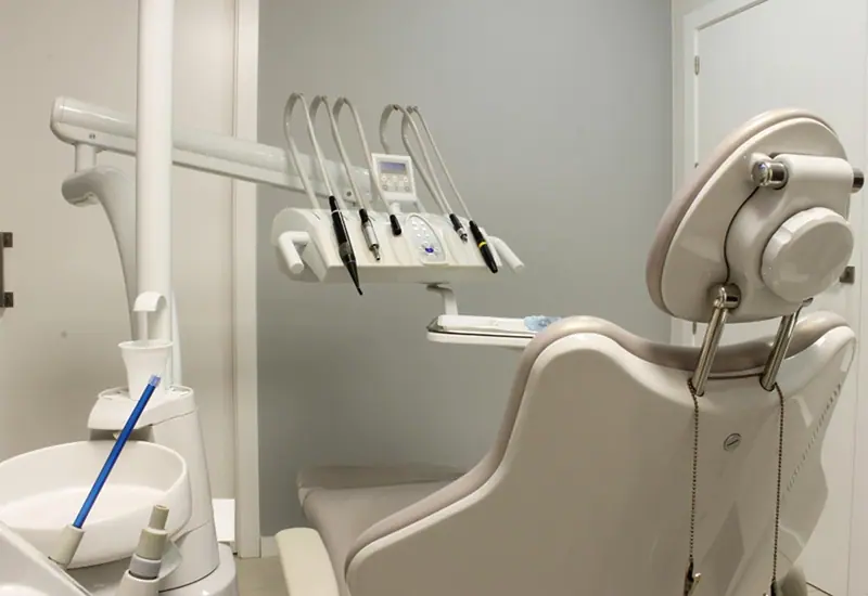 Equipo odontológico com instrumentos e cadeira bege numa sala de atendimento