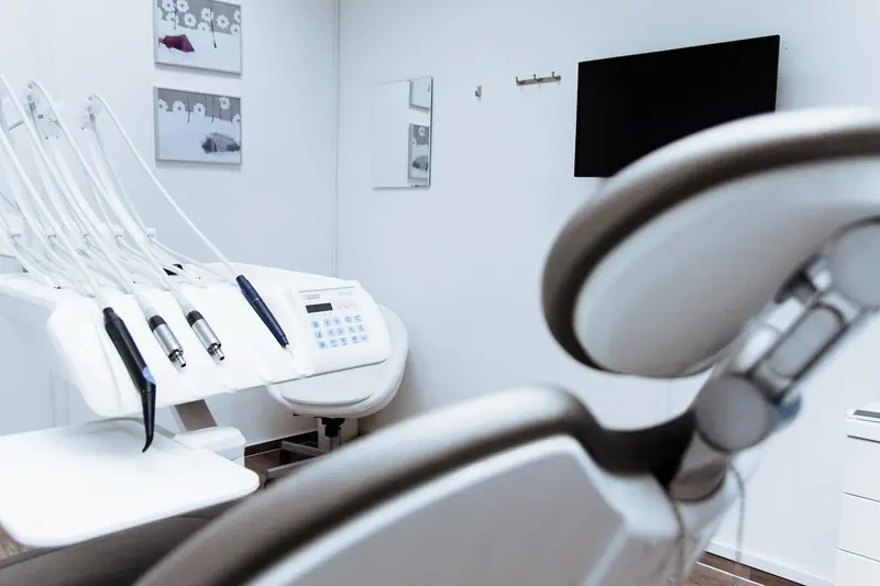 Peças de mão odontológicas encaixadas no suporte ao lado da cadeira, em consultório branco