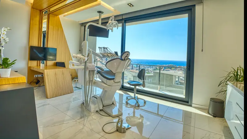 Consultório odontológico moderno, com cadeira clara, iluminação embutida e uma grande janela de vidro