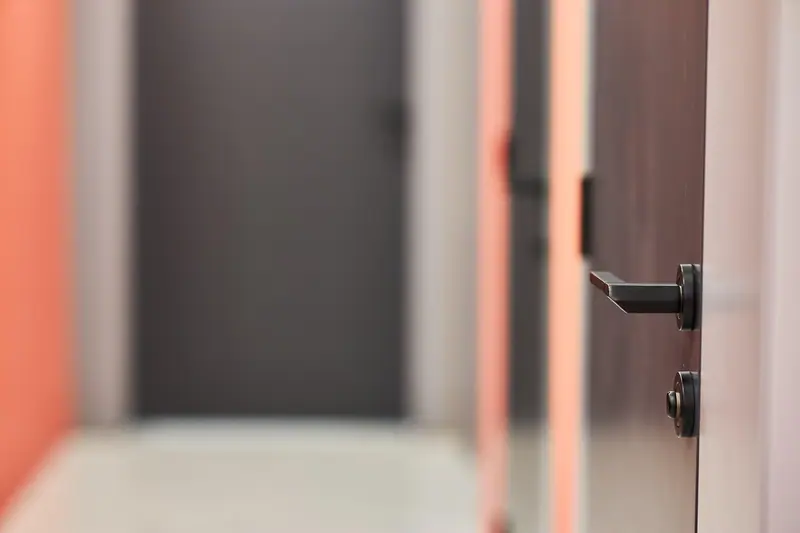 Maçaneta preta de uma porta escura, com um corredor desfocado ao fundo