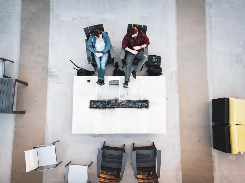 Vista de cima de duas pessoas conversando sentadas em poltronas num espaço de convivência