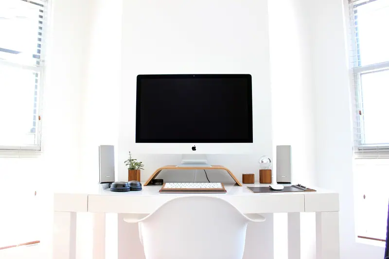 Mesa branca com monitor e caixas de som num escritório claro e organizado