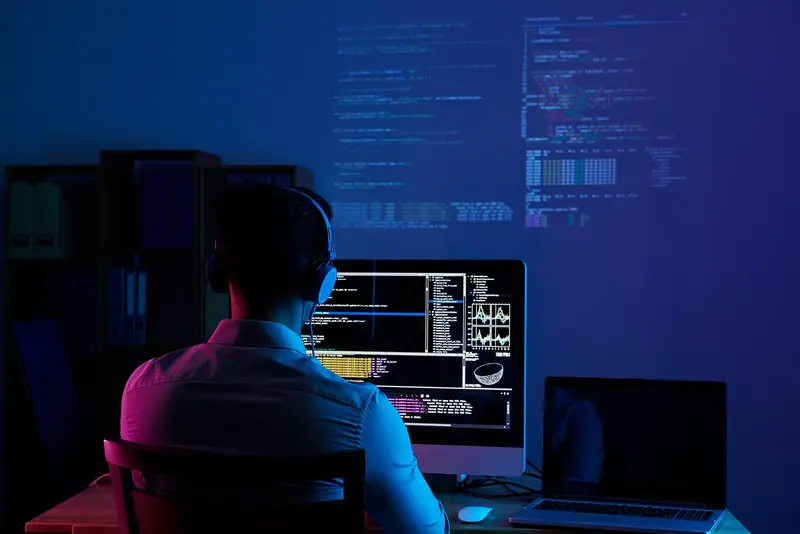 Pessoa de costas trabalhando diante de monitores num ambiente iluminado de azul