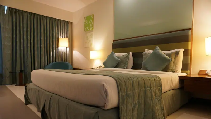 Quarto de casal com luz baixa e cortina pesada verde-acinzentada ao lado da cama