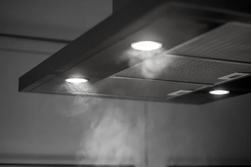 Coifa de cozinha com luzes acesas puxando o vapor que sobe, em preto e branco