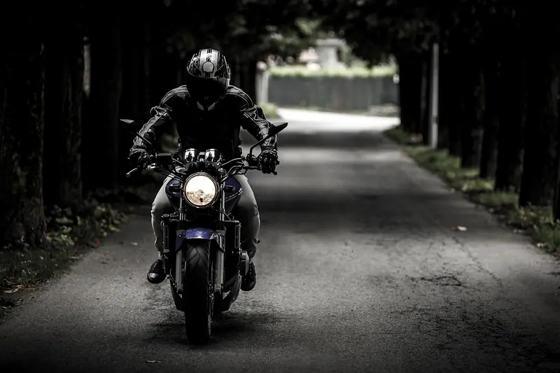 Motociclista de capacete vindo pela rua escura, com o farol da moto aceso