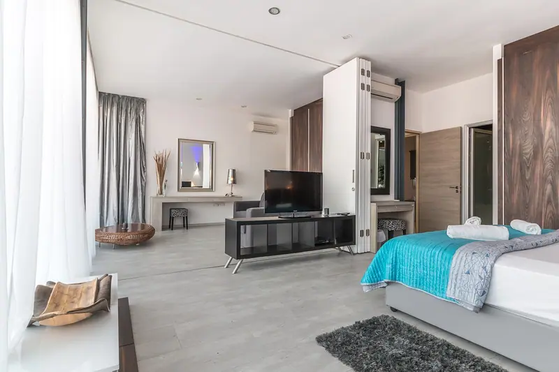 Quarto amplo e claro, com cama, móveis baixos e cortinas longas cobrindo uma janela grande