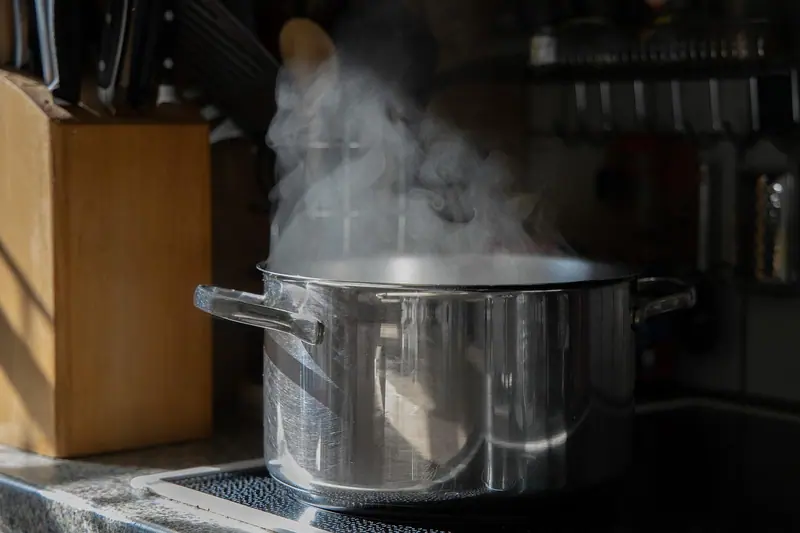 Panela de inox soltando vapor sobre o fogão, ao lado de um bloco de facas de madeira