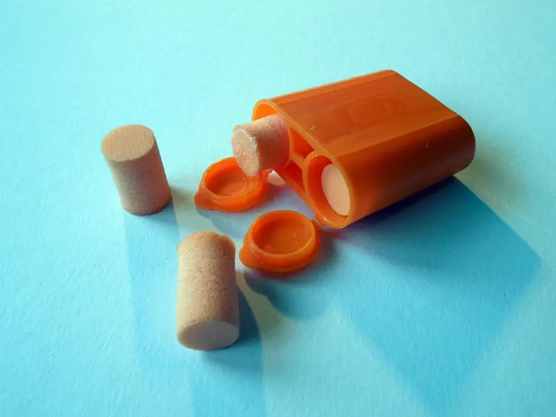 Protetores auriculares de espuma ao lado de um estojo laranja aberto sobre fundo azul
