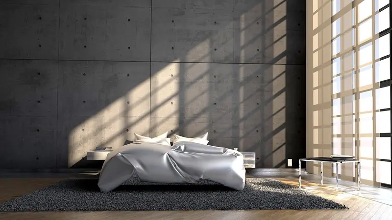 Cama desarrumada num quarto de parede de concreto, com faixas de sol entrando pela persiana