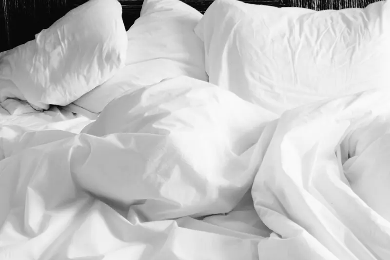 Lençóis e travesseiros brancos amarrotados numa cama arrumada às pressas