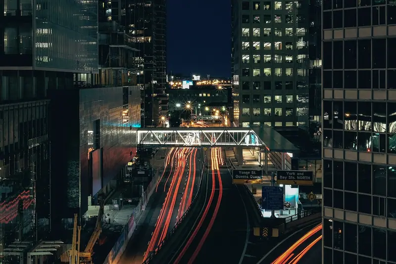 Rastros de luz dos carros numa avenida entre prédios de escritórios, à noite