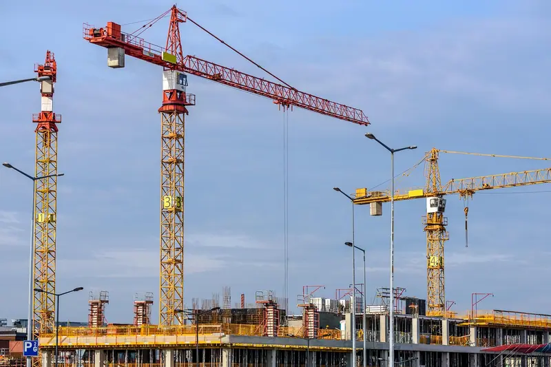 Guindastes sobre um prédio em construção, com o céu azul ao fundo