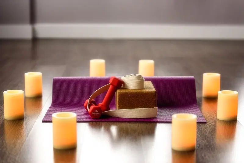 Tapete de yoga roxo com bloco e faixa, cercado por velas acesas sobre piso de madeira