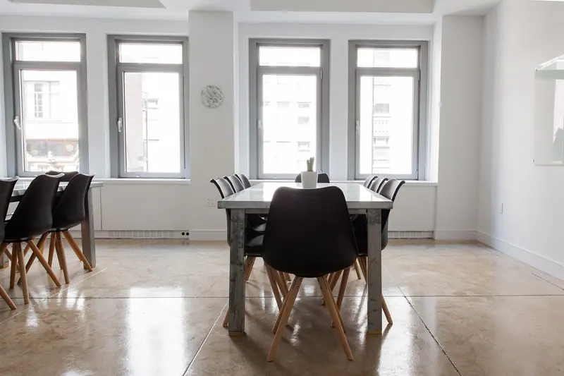 Sala de jantar clara com mesa, cadeiras pretas e quatro janelas voltadas para a rua