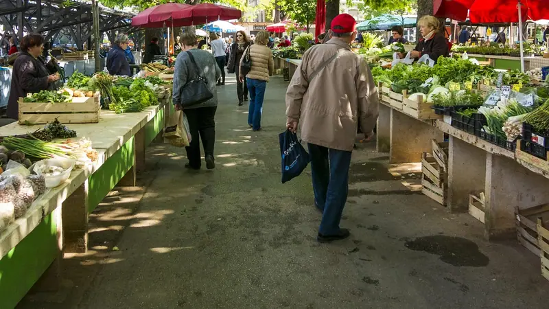 Rua com barracas de feira cobertas por toldos e pessoas caminhando entre as bancas de verduras