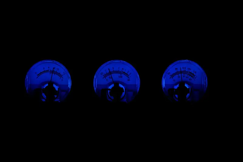 Três mostradores analógicos de nível de som iluminados em azul num fundo escuro
