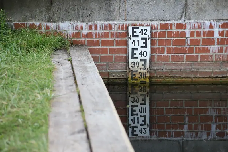 Régua numerada presa a uma parede de tijolos, refletida na água de um canal
