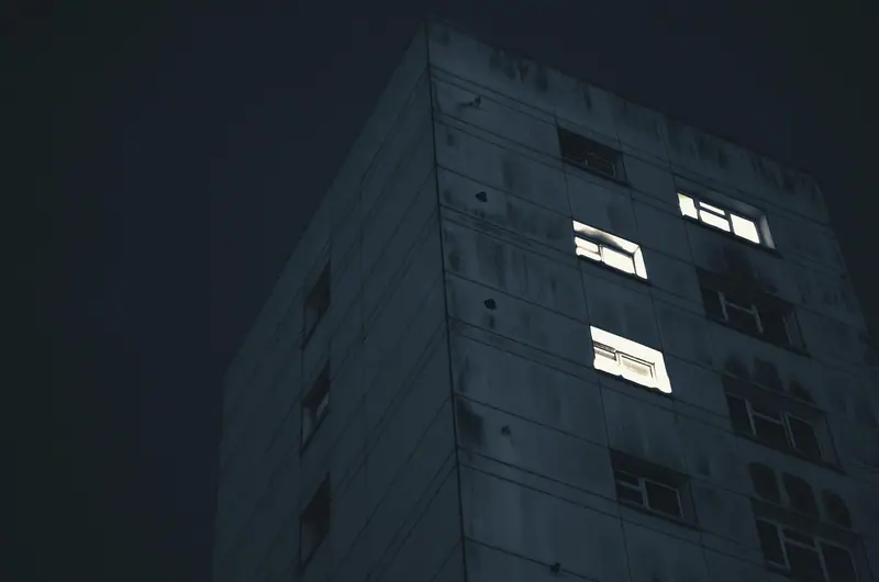 Fachada de prédio no escuro, com poucas janelas acesas durante a noite