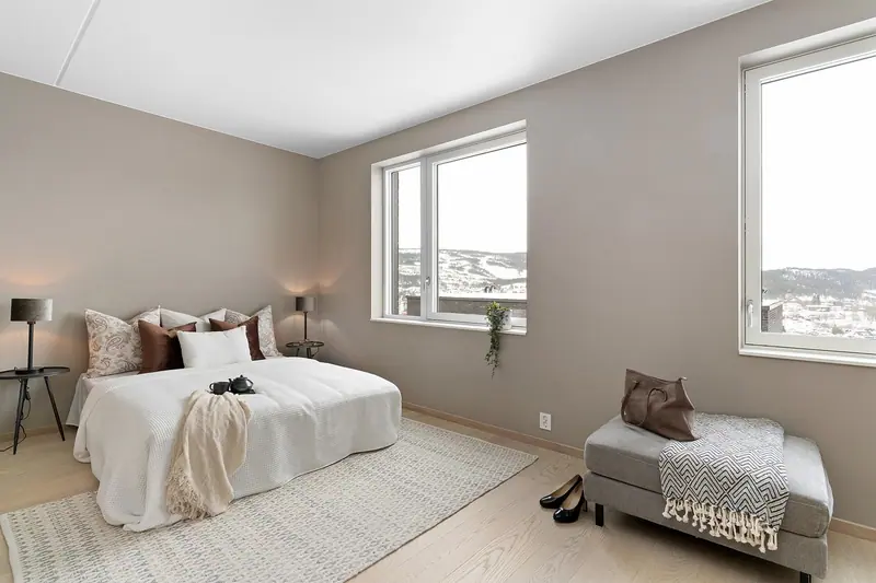 Quarto claro com cama de casal arrumada, banco ao pé da cama e janela com vista para a cidade