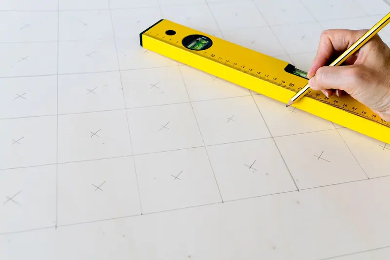 Mão marcando uma linha a lápis com a ajuda de um nível amarelo sobre uma superfície clara