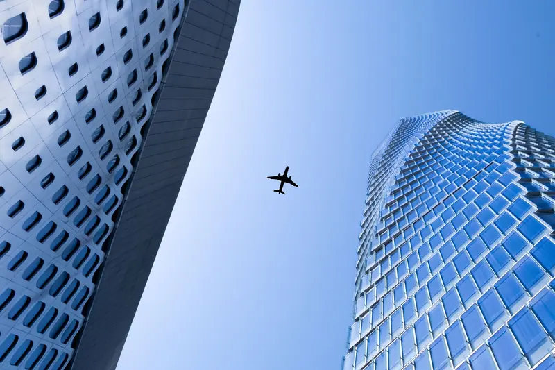 Avião passando no céu entre duas torres envidraçadas, visto de baixo