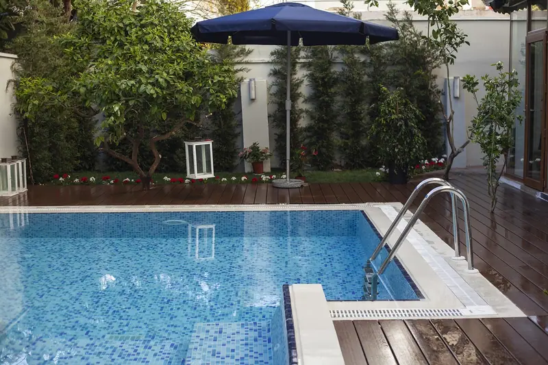 Piscina com deck de madeira, guarda-sol e jardim, numa área de lazer residencial
