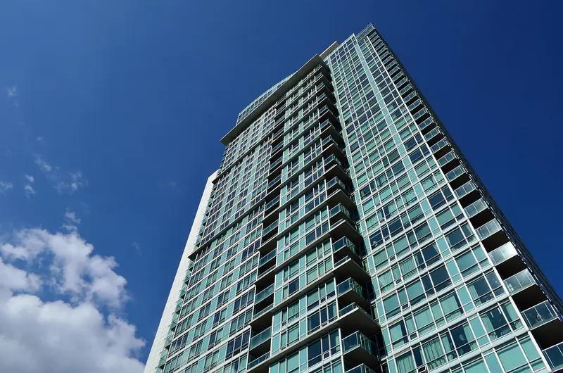 Torre residencial alta com fachada de vidro e varandas, vista de baixo contra o céu azul