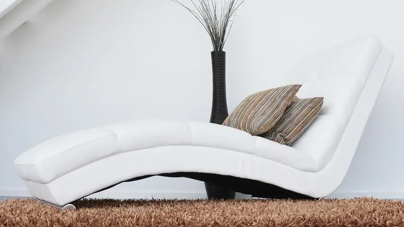 Divã branco com duas almofadas listradas numa sala clara, ao lado de um vaso alto