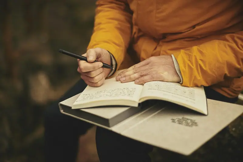 Mãos de uma pessoa segurando uma caneta sobre um livro aberto no colo