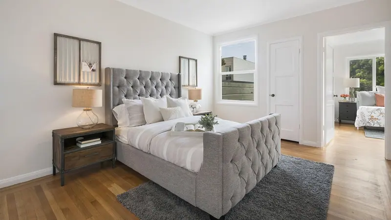 Quarto com cama estofada, janela na parede lateral e porta aberta para outro cômodo