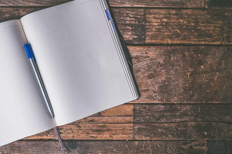 Caderno aberto com páginas pautadas e uma caneta azul sobre uma mesa de madeira escura