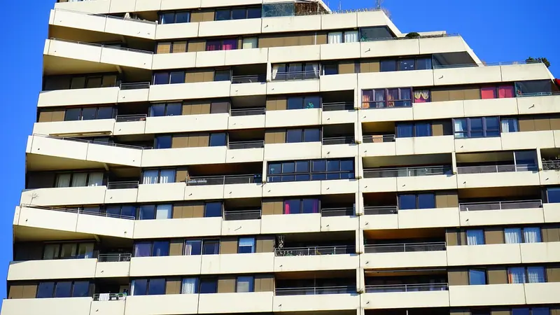 Prédio residencial alto de cor clara, com faixas de varandas em todos os andares, contra o céu azul