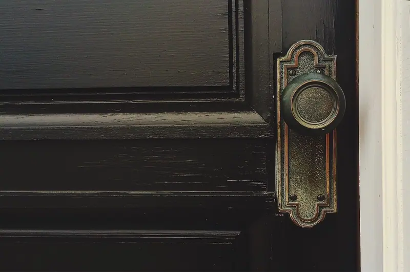 Detalhe de uma porta de madeira escura com maçaneta antiga de metal