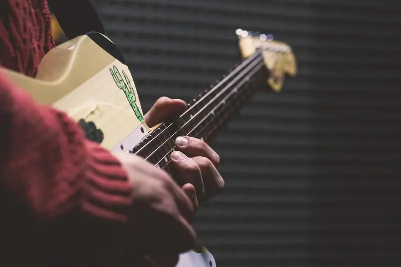 Mãos tocando um contrabaixo diante de uma parede escura coberta de espuma