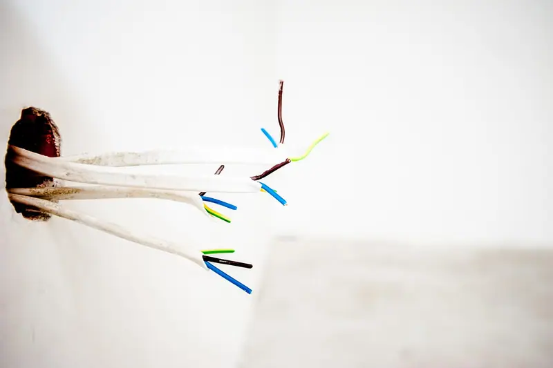 Fios elétricos saindo de um furo numa parede branca