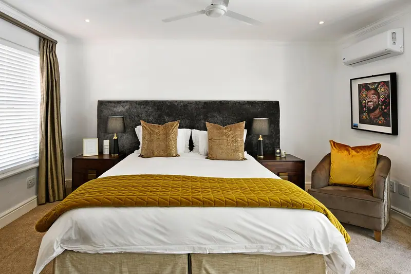 Quarto de casal com cabeceira escura, cortinas e ar-condicionado split no alto da parede