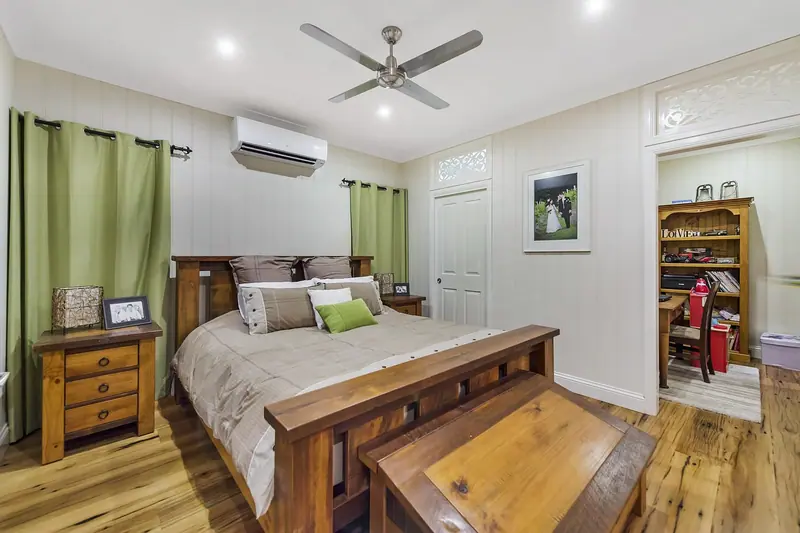 Quarto com cama de madeira, cortinas verdes, ventilador de teto e ar-condicionado split na parede