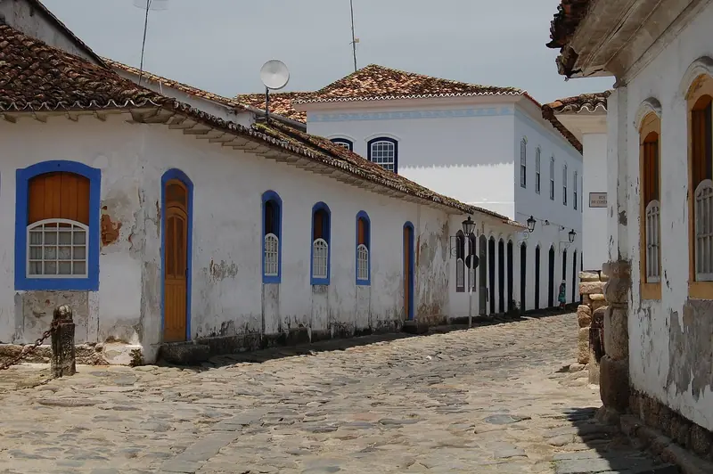 Casas térreas brancas com janelas azuis e portas de madeira rente à calçada de pedra