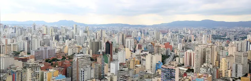 Vista ampla de prédios de São Paulo num dia claro, com serras ao fundo