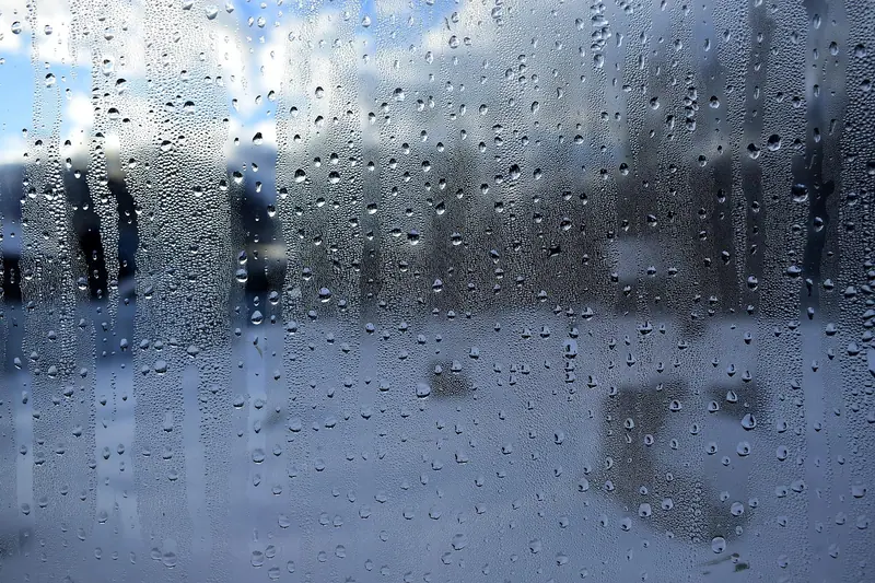 Vidro de janela coberto de gotas de chuva, com pessoas desfocadas na rua do lado de fora