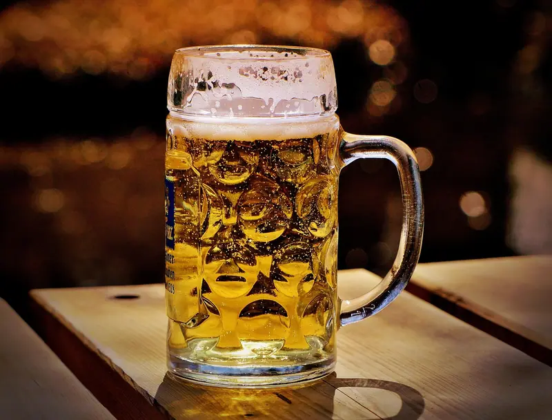 Caneca de chope cheia sobre uma mesa de madeira, com luzes desfocadas ao fundo
