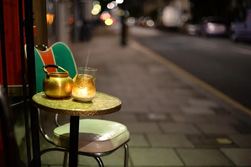 Mesa redonda com copo e vela na calçada de uma rua à noite