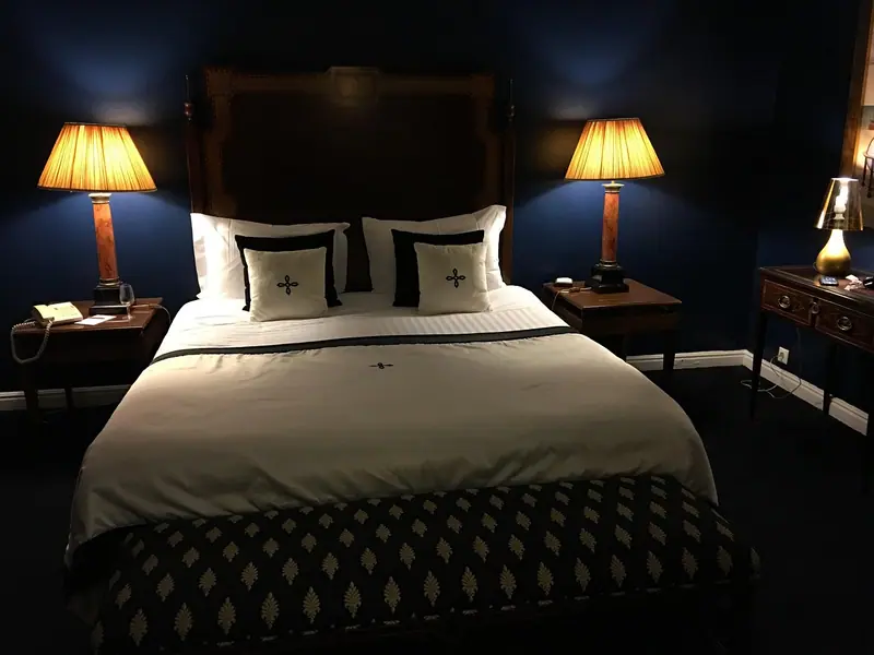 Quarto à noite com cama arrumada e dois abajures acesos ao lado da cabeceira