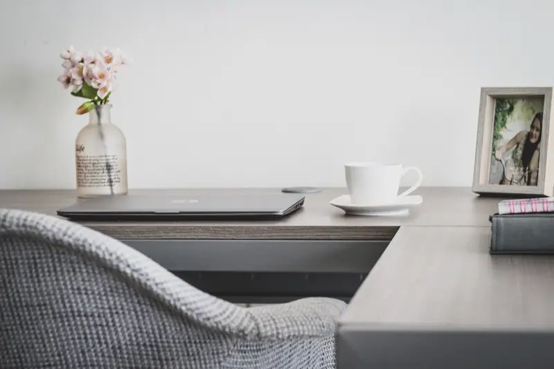 Mesa de trabalho em casa com notebook, xícara de café e um vaso de flores