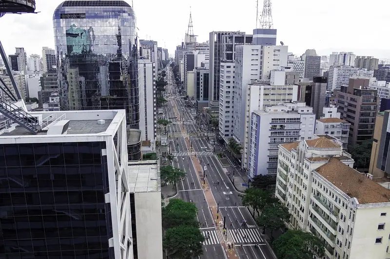Avenida larga com carros, vista do alto de um prédio, entre edifícios altos