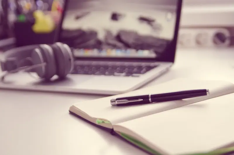 Fone de ouvido ao lado de um notebook e de um caderno com caneta sobre a mesa